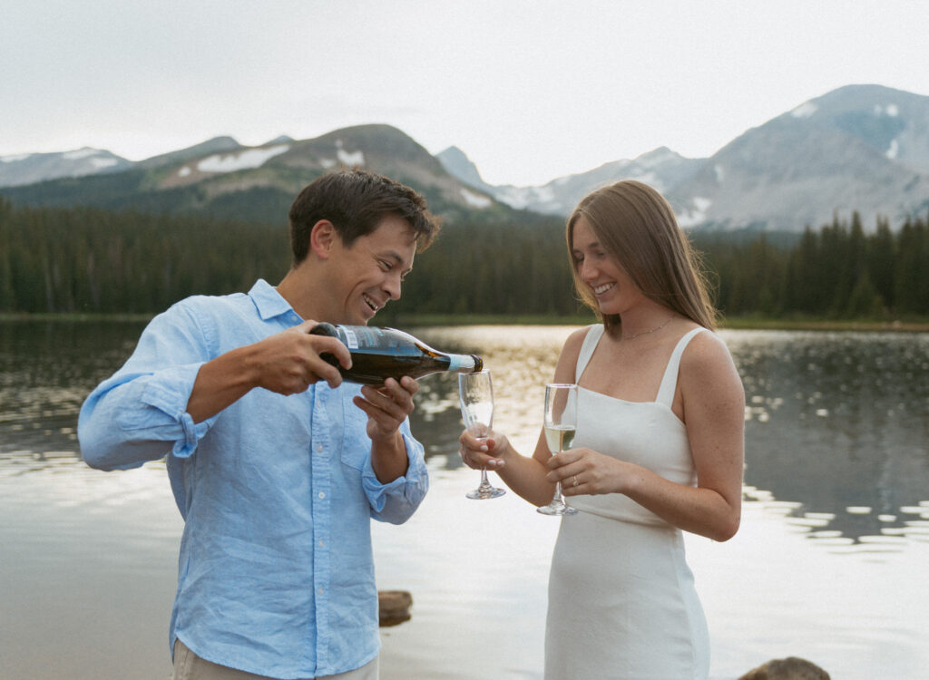 A couple pouring champagne to celebrate their Brainard Lake engagement session