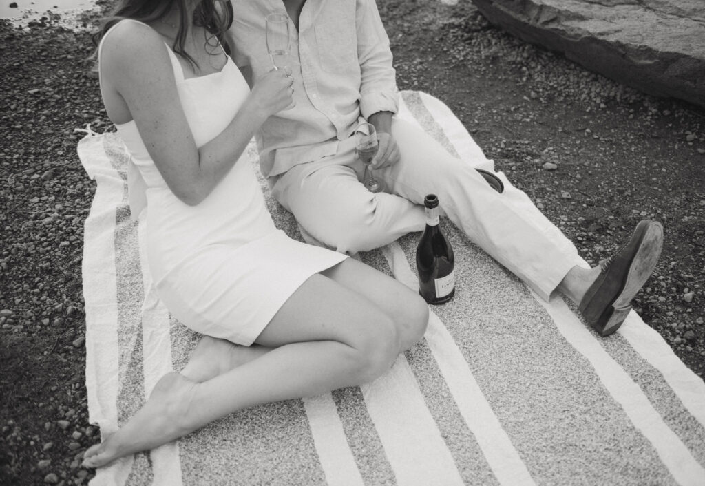 A couple sitting side by side on a blanket sipping champagne