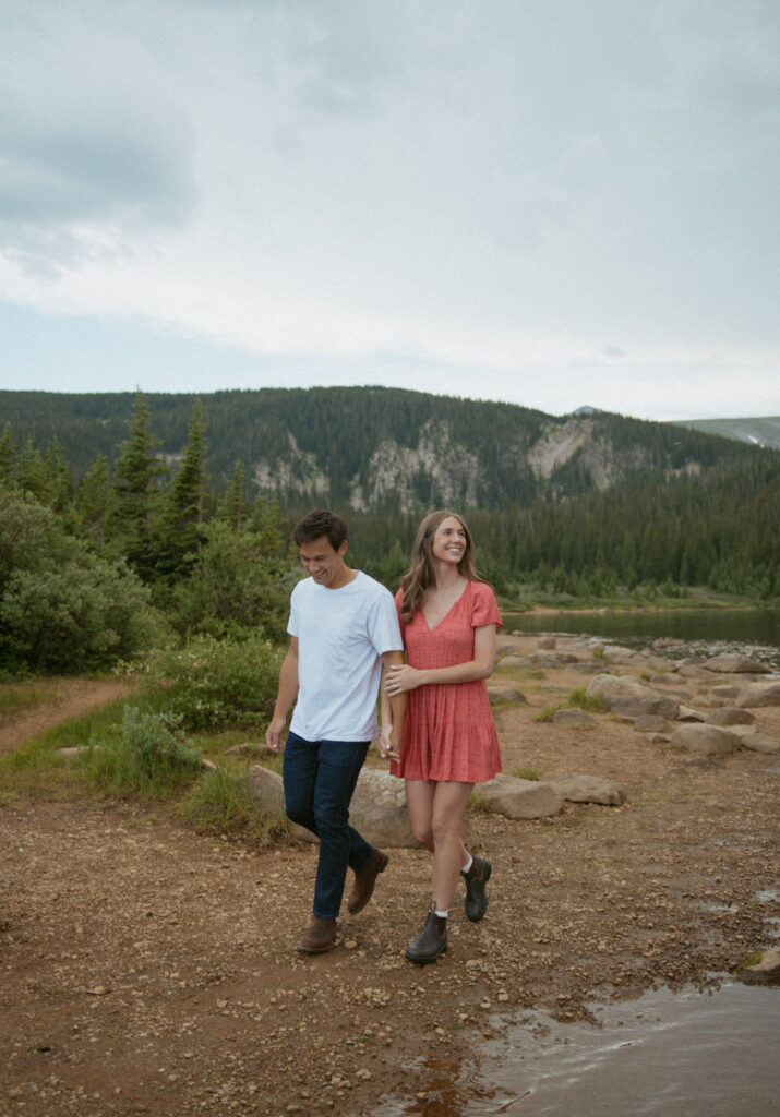 A couple walking arm in arm along the shore of a lake during their engagement session