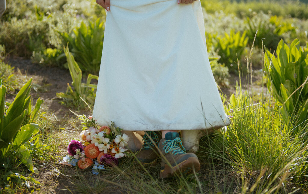 A bride shows off her hiking boots under her wedding dress, next to her colorful bouquet