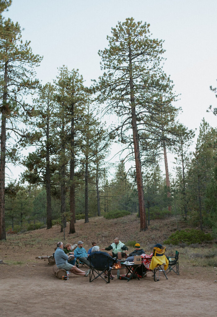 a couple enjoys a bonfire at a camp site with their family and friends the night before their wedding