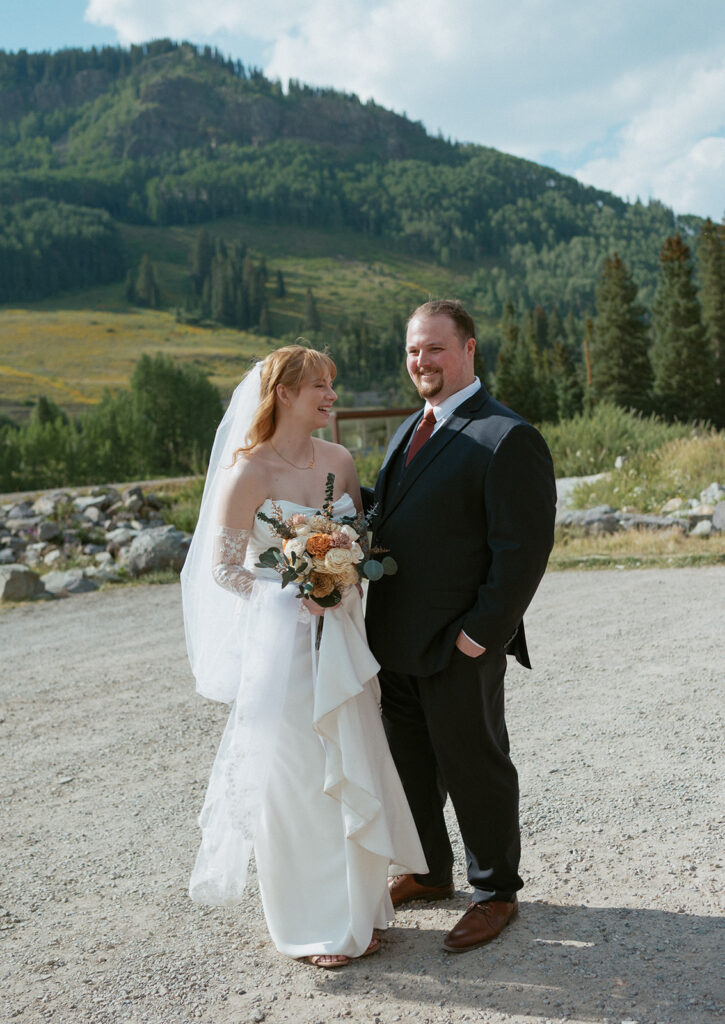 a couple stands together smiling in the mountains after getting married